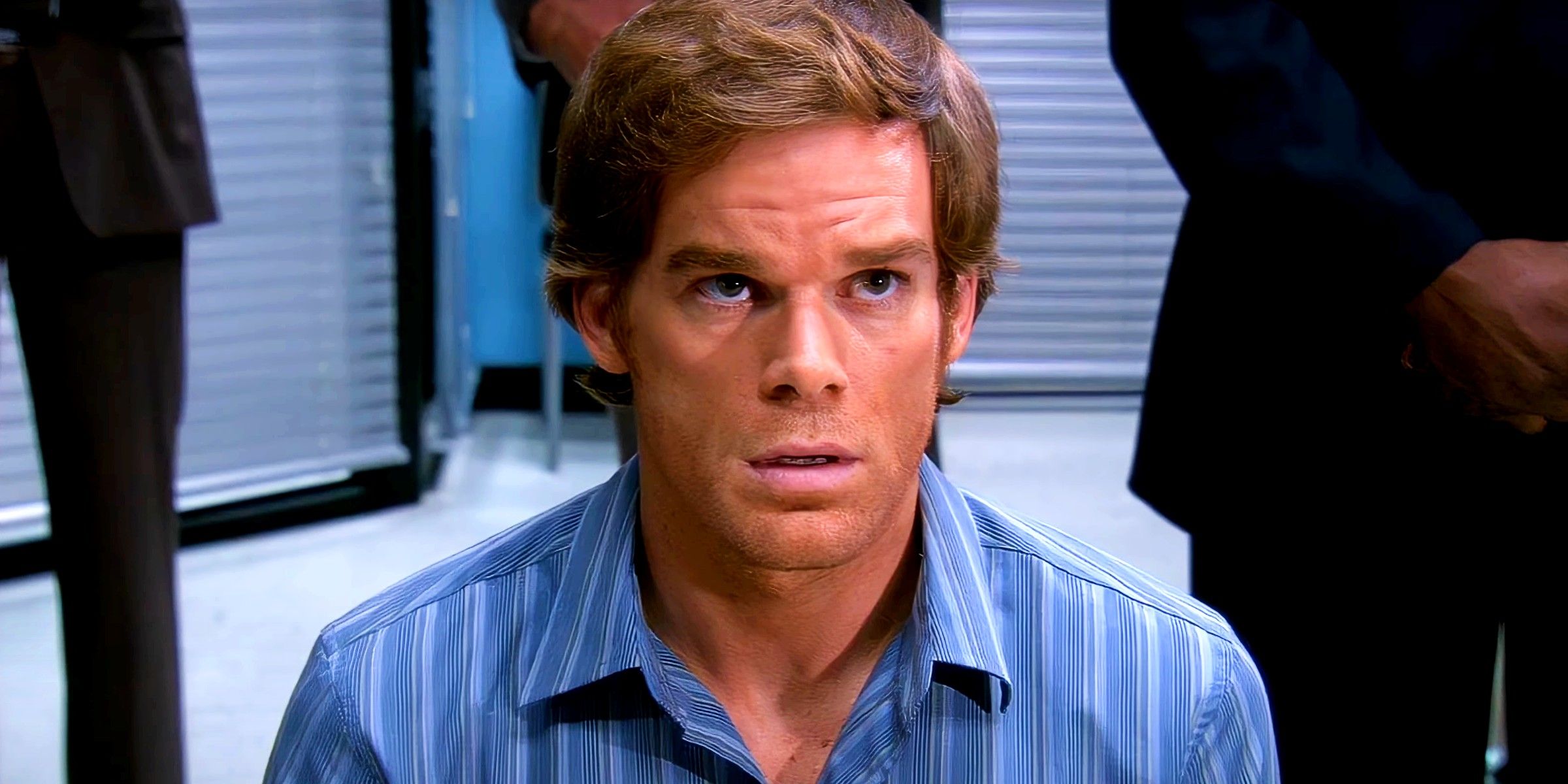 Dexter Morgan looking nervous staring up at a figure with people behind him in Dexter season 2
