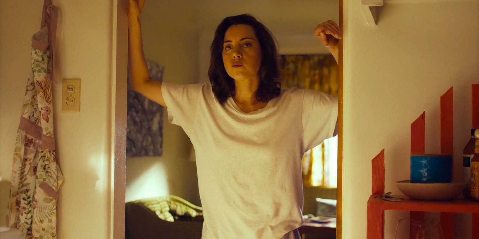 MG (Aubrey Plaza) leaning against the door frame in Honey Don't!