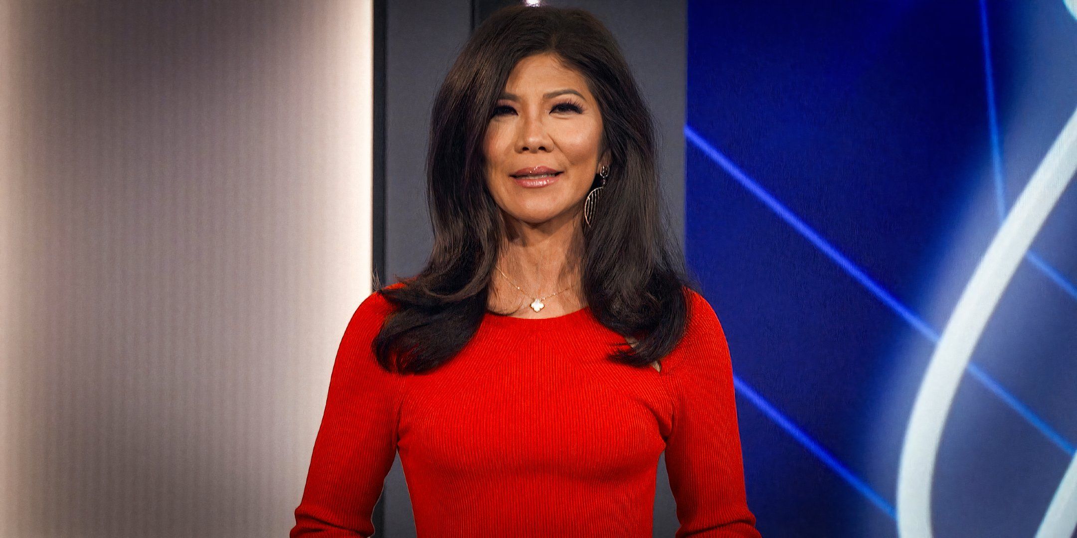 Big Brother host Julie Chen Moonves in a red top standing on the show's stage.