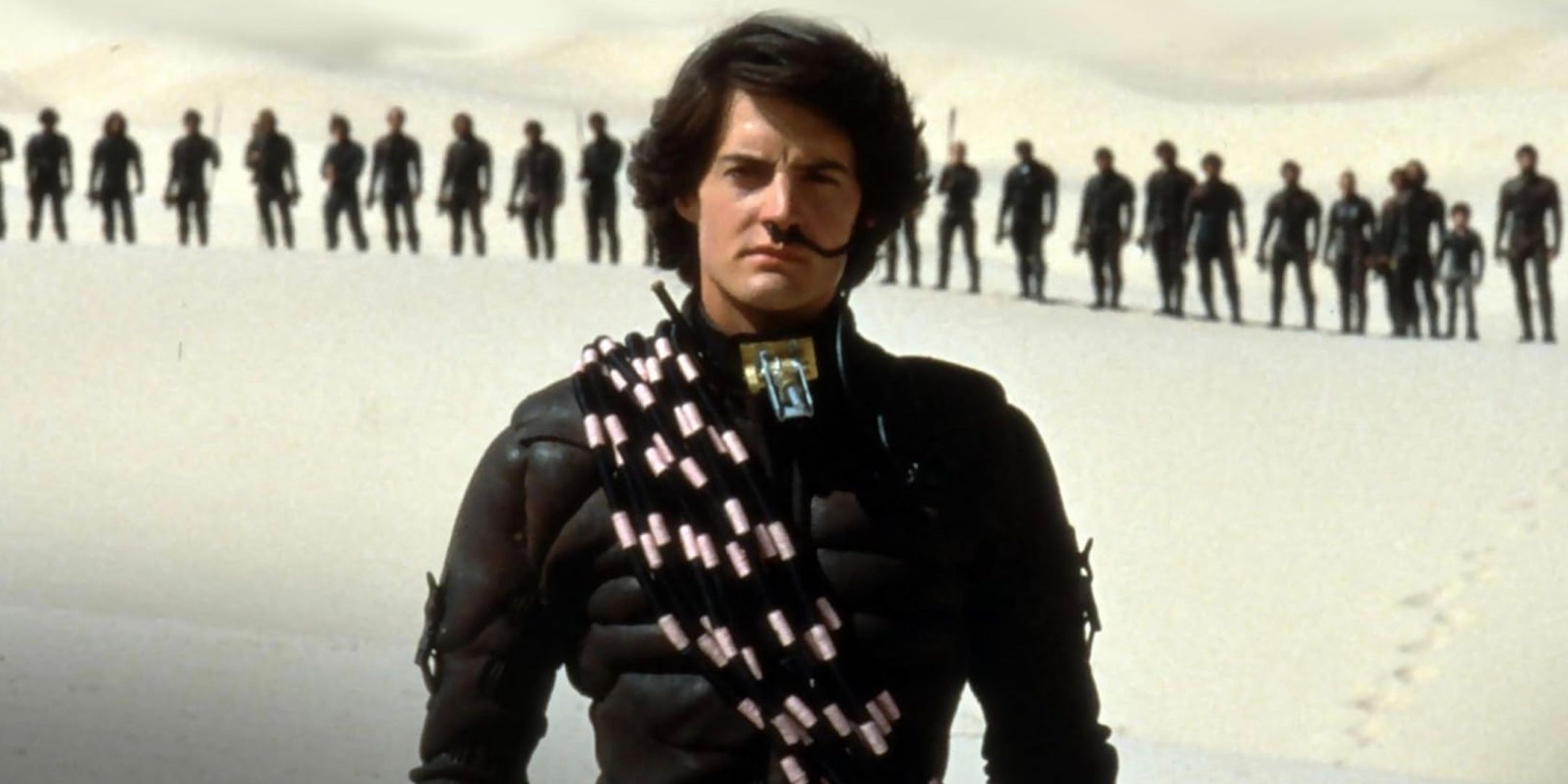 Kyle MacLachlan stands in front of a line of uniformed figures. 