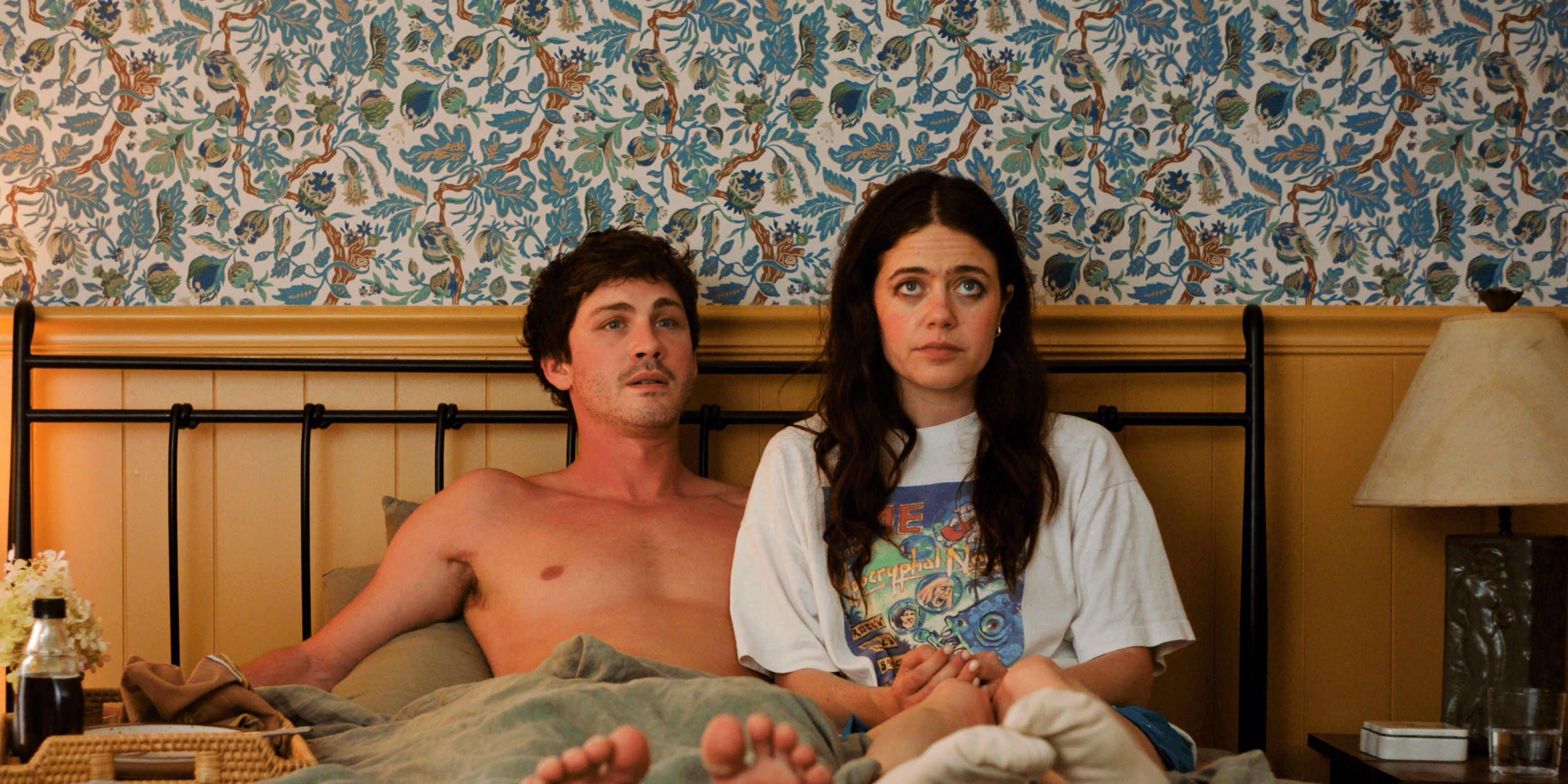 Logan Lerman and Molly Gordon sitting on a bed with uneasy expressions in Oh Hi