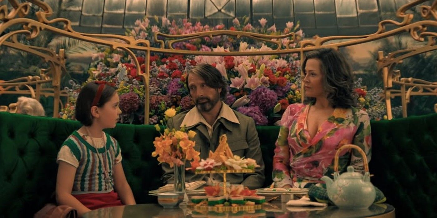 Mads Mikkelsen and Sigourney Weaver sit at a tea table with a young girl in Dust Bunny