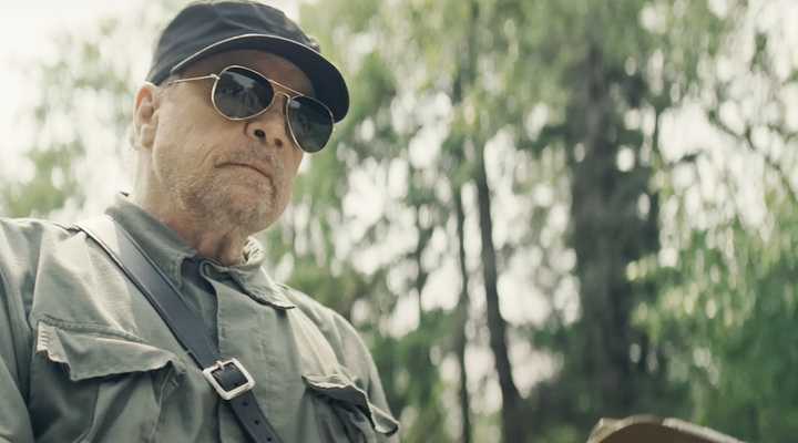 Mark Hamill wears aviator glasses and looks menacing in a scene from The Long Walk