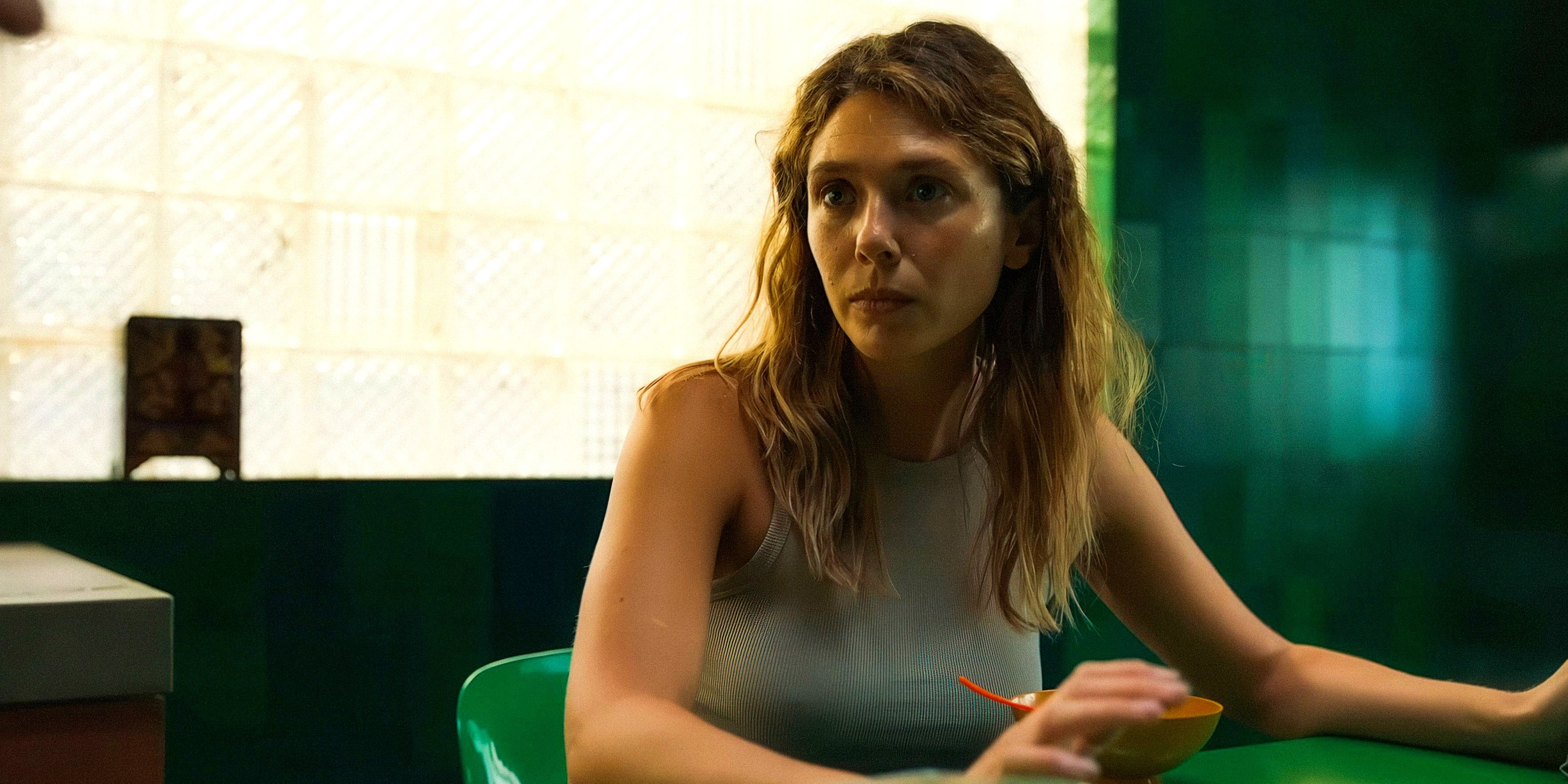 Mia (Elizabeth Olsen) sits at a table with a frustrated expression in The ᴀssessment