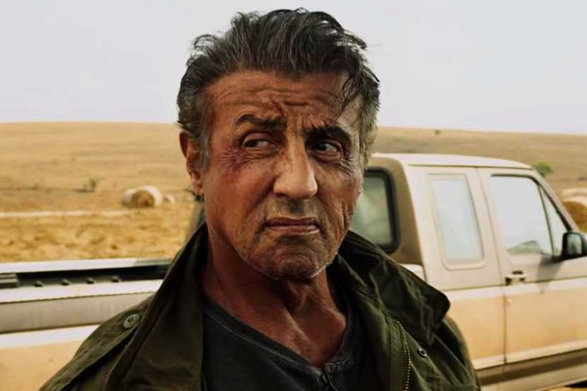 Rambo looks over his shoulder with a scowl in front of his truck in Rambo: Last Blood