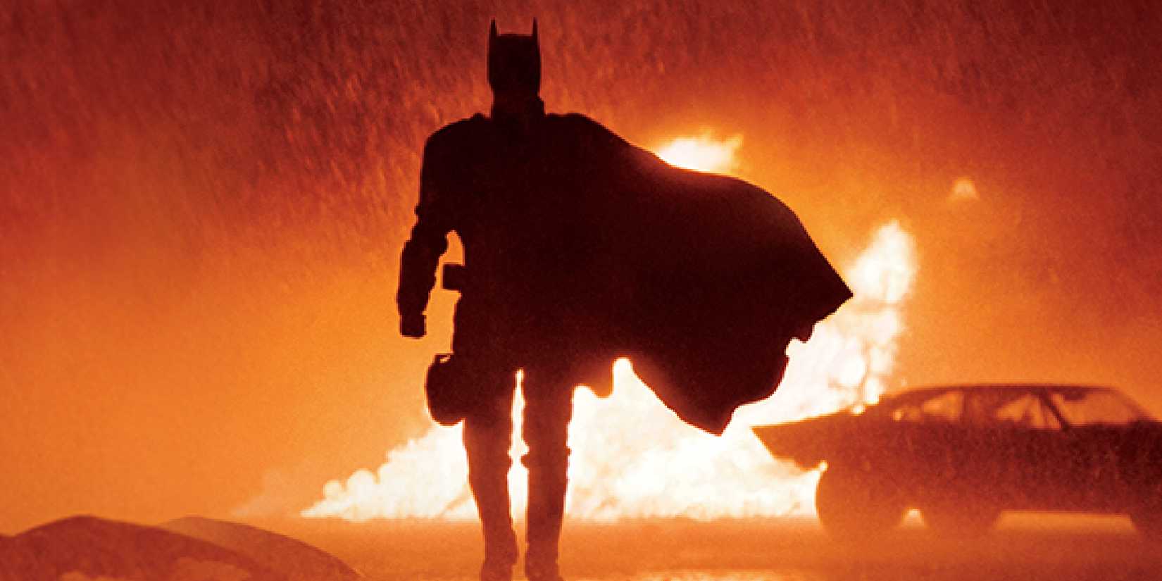 Robert Pattinson's Batman walks in front of fire in the rain in Matt Reeves' The Batman