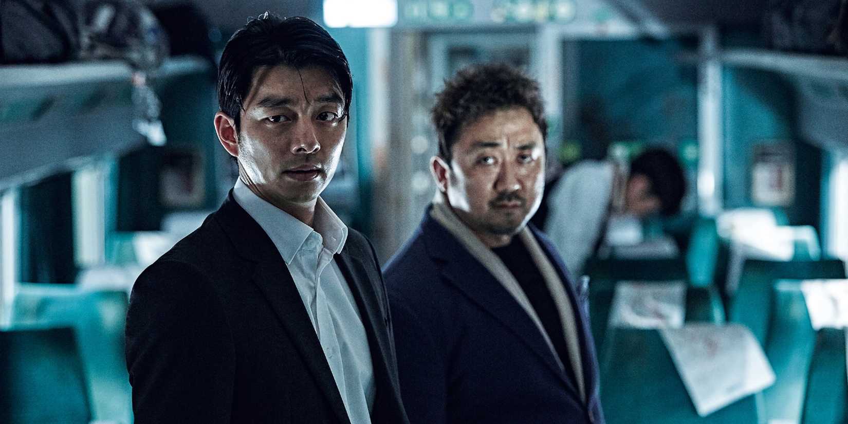 Seok-woo and Sang-wa look on with concerned expressions while standing in the aisle of the train in Train to Busan