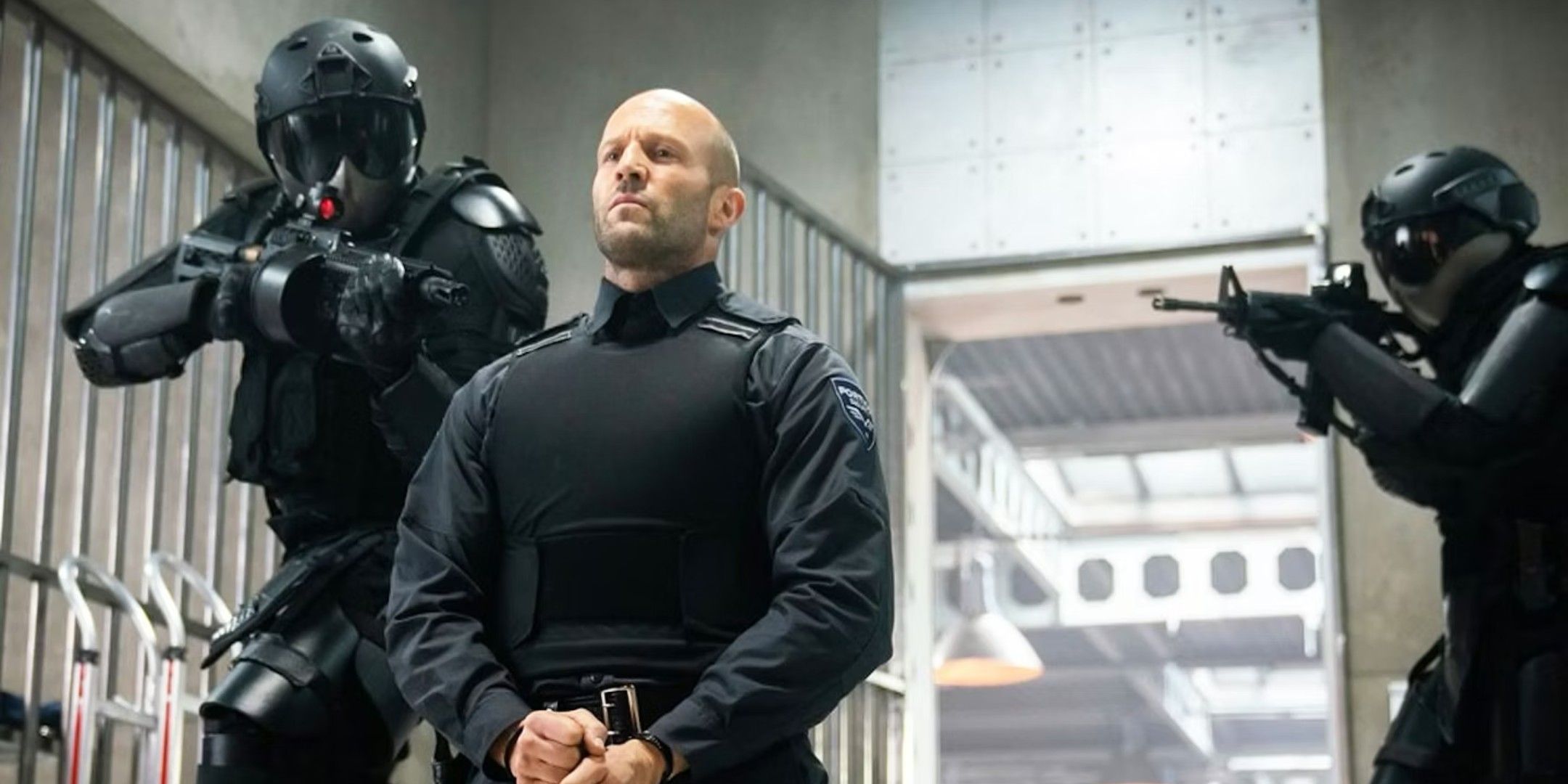 Jason Statham kneels as two armed guards point guns at him in Wrath of Man