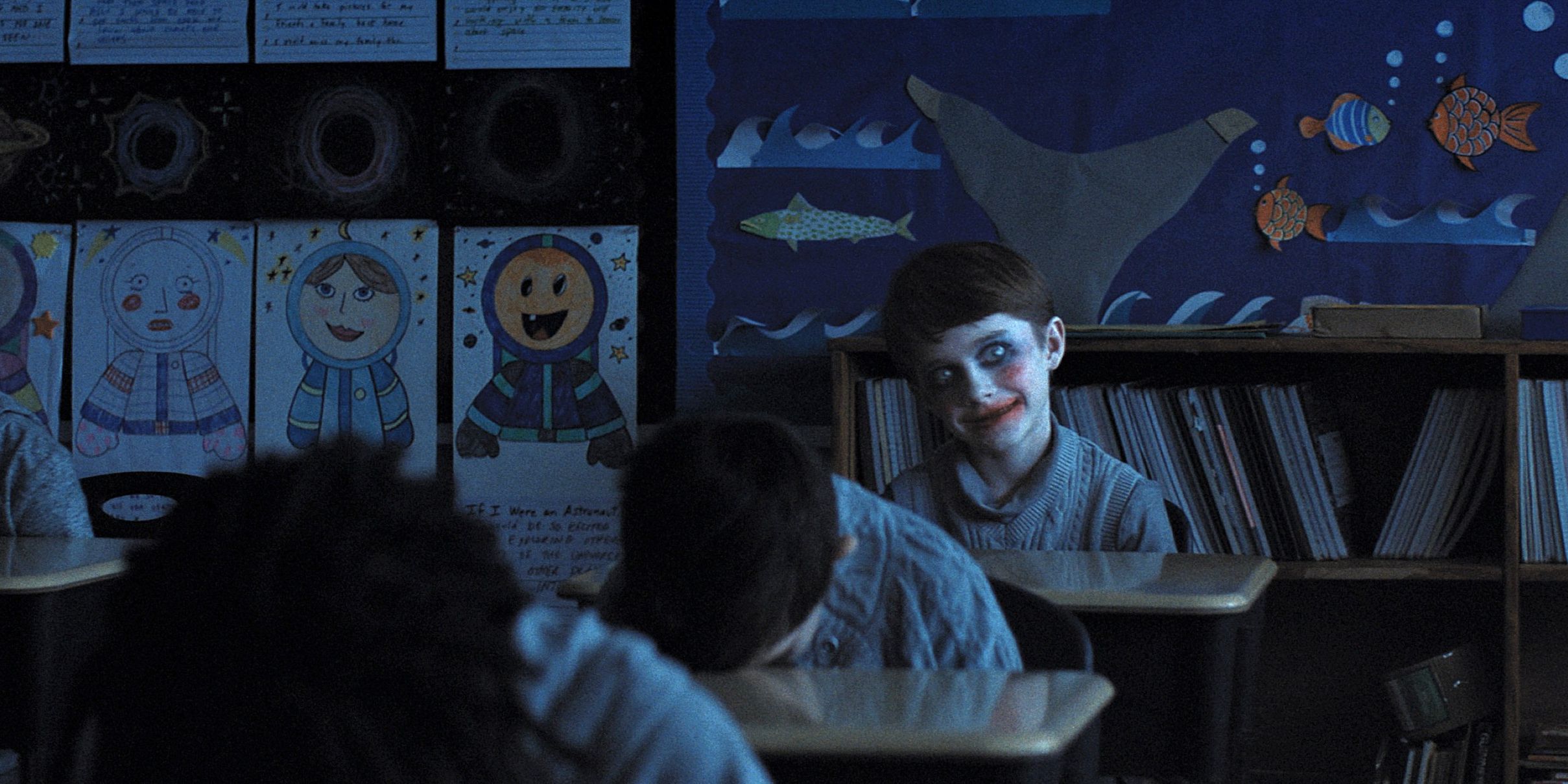 Alex smiling in overdone makeup as classmates sleep on their desks in Weapons