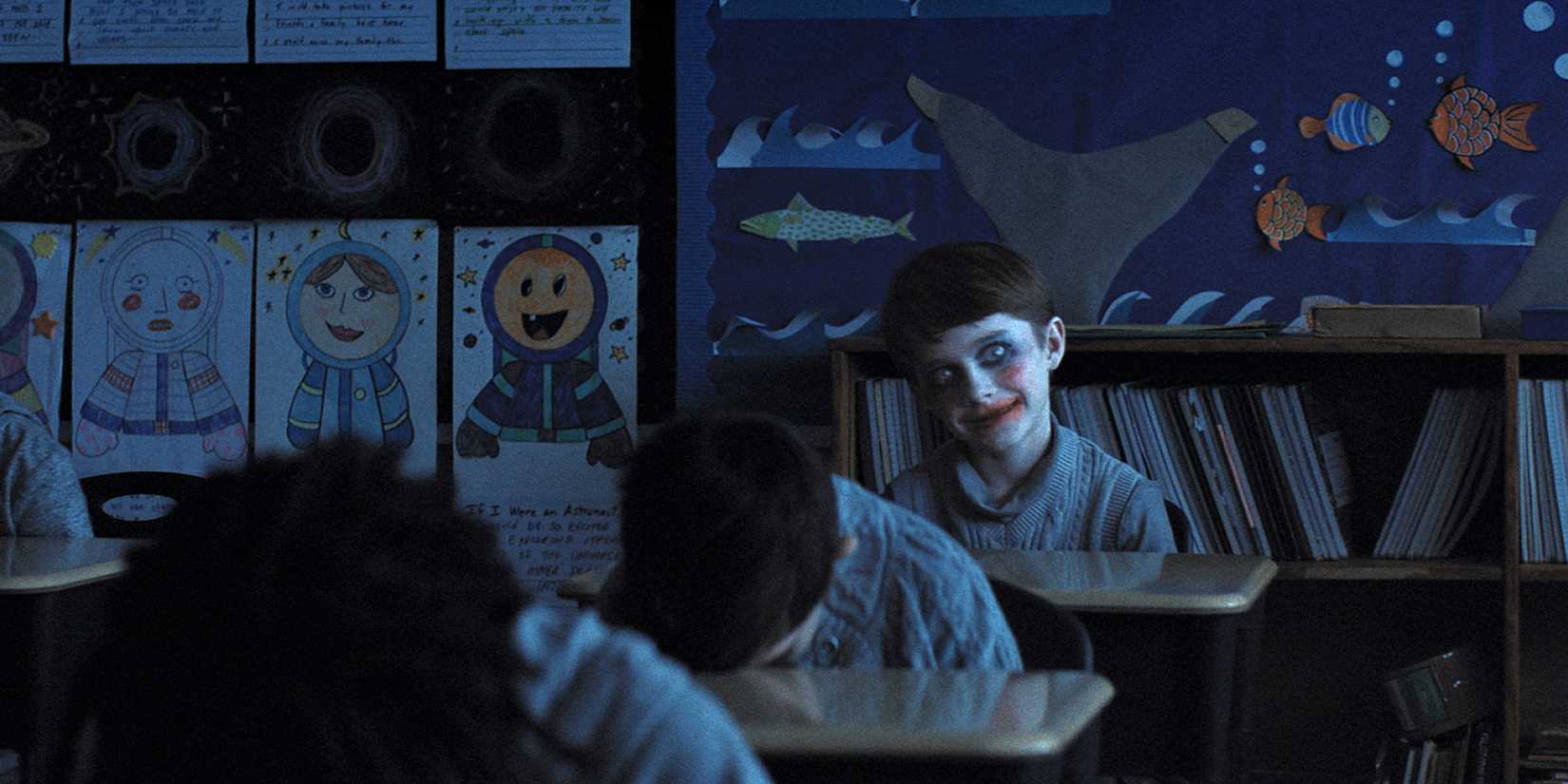 Alex smiling in overdone makeup as classmates sleep on their desks in Weapons