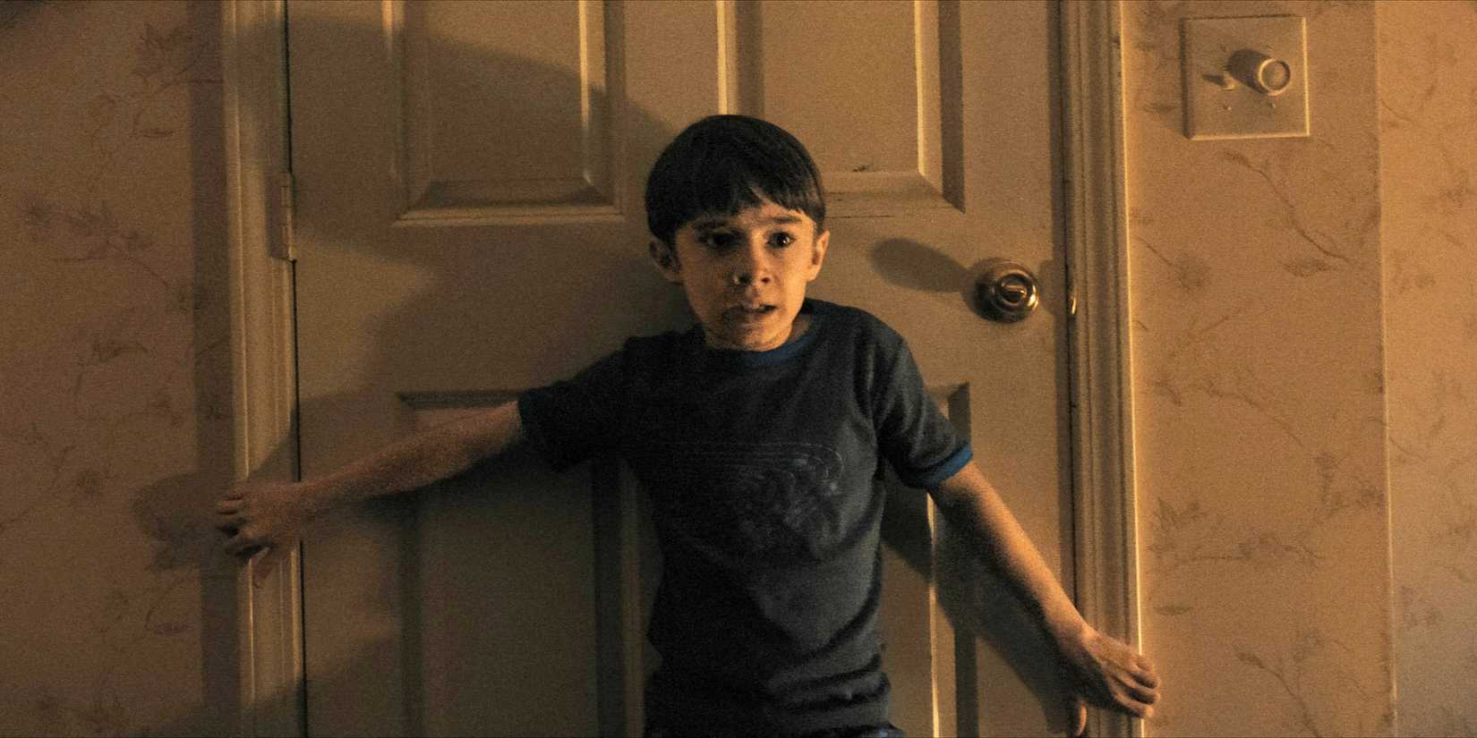 Alex standing in front of a door, clutching the frame, with a terrified expression in Weapons