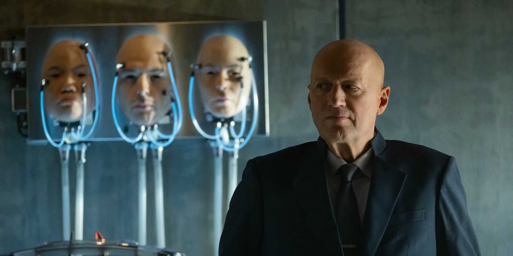 Ade Edmondson as Atom Eins. standing next to some prosthetic heads in Alien: Earth Episode 4