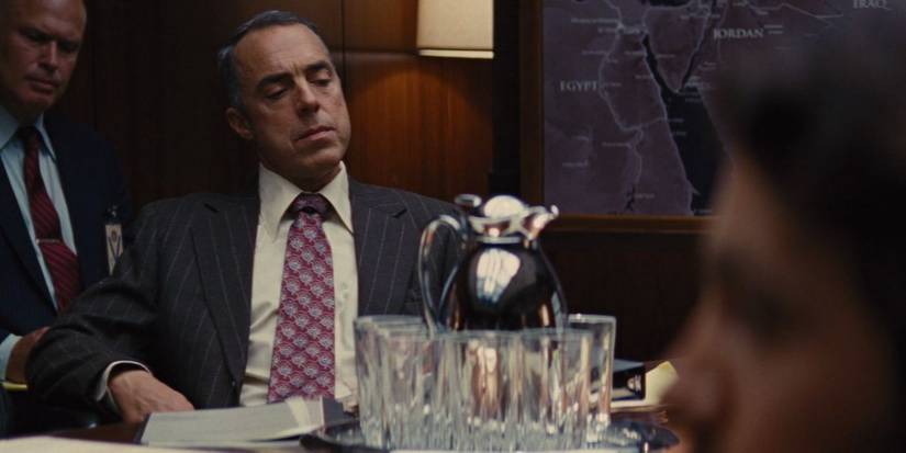 Titus Welliver looks on while sitting in front of a map of Iran in Argo