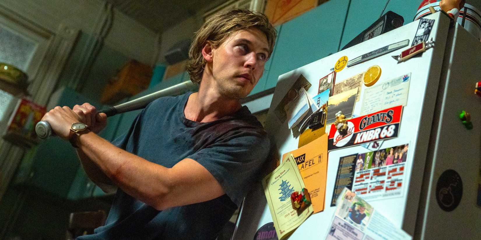 Austin Butler holding a baseball bat while standing next to a fridge in Caught Stealing