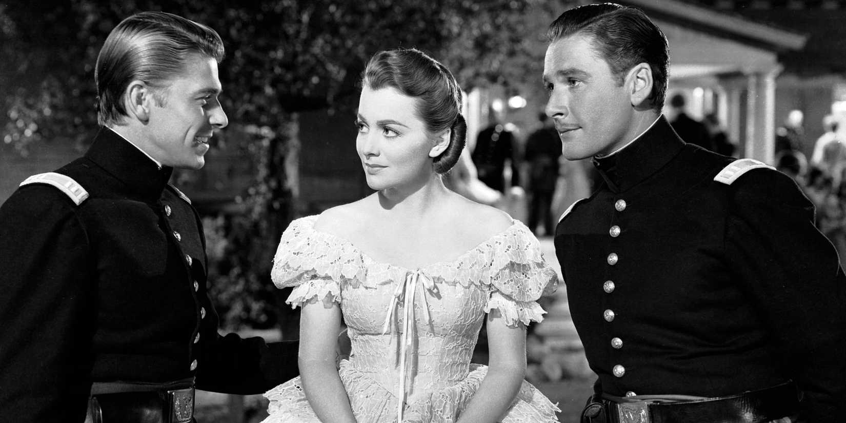 Errol Flynn as James and Olivia de Haviland as Kit talking to Raymond Mᴀssey as John in Santa Fe Trail