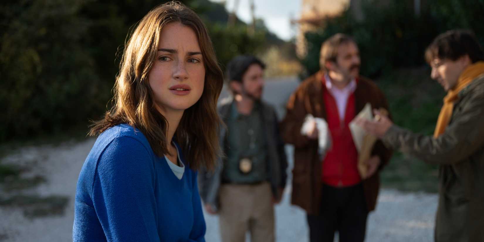 Grace Van Patten's Amanda looking worried while Raffaele talks with two cops in the background in The Twisted Tale of Amanda Knox