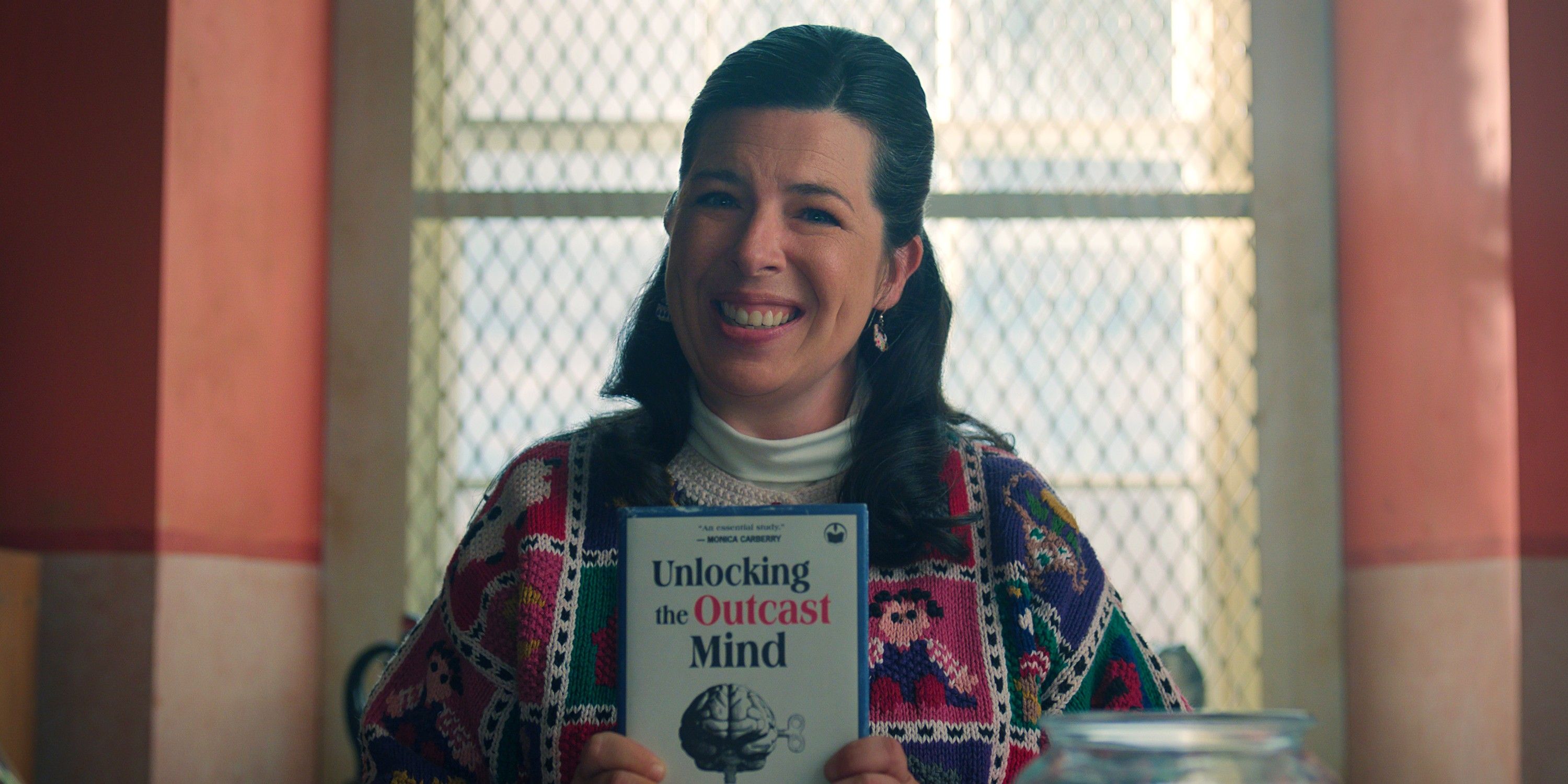 Heather Matarazzo as Judi smiling and holding up a book in Wednesday season 2