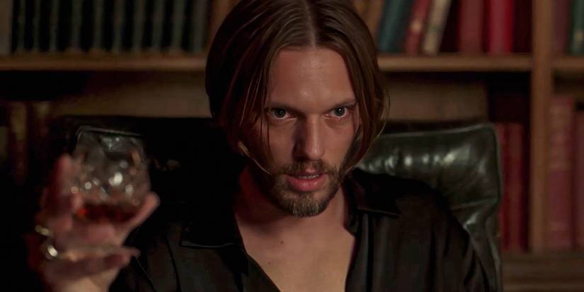 Jamie Campbell Bower giving an intense look while holding a brandy snifter in Witchboard 2025