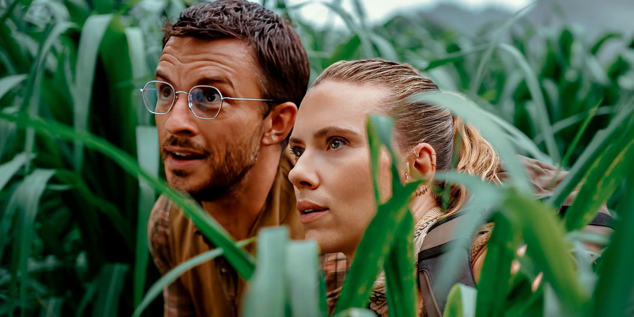 Scarlett Johansson and Jonathan Bailey kneeling in tall grᴀss in Jurᴀssic World Rebirth.