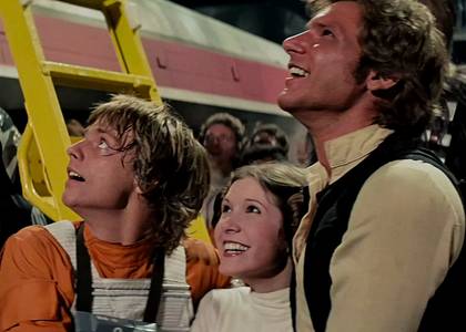 Luke Leia and Han Solo arm in arm and smiling at the end of Star Wars A New Hope