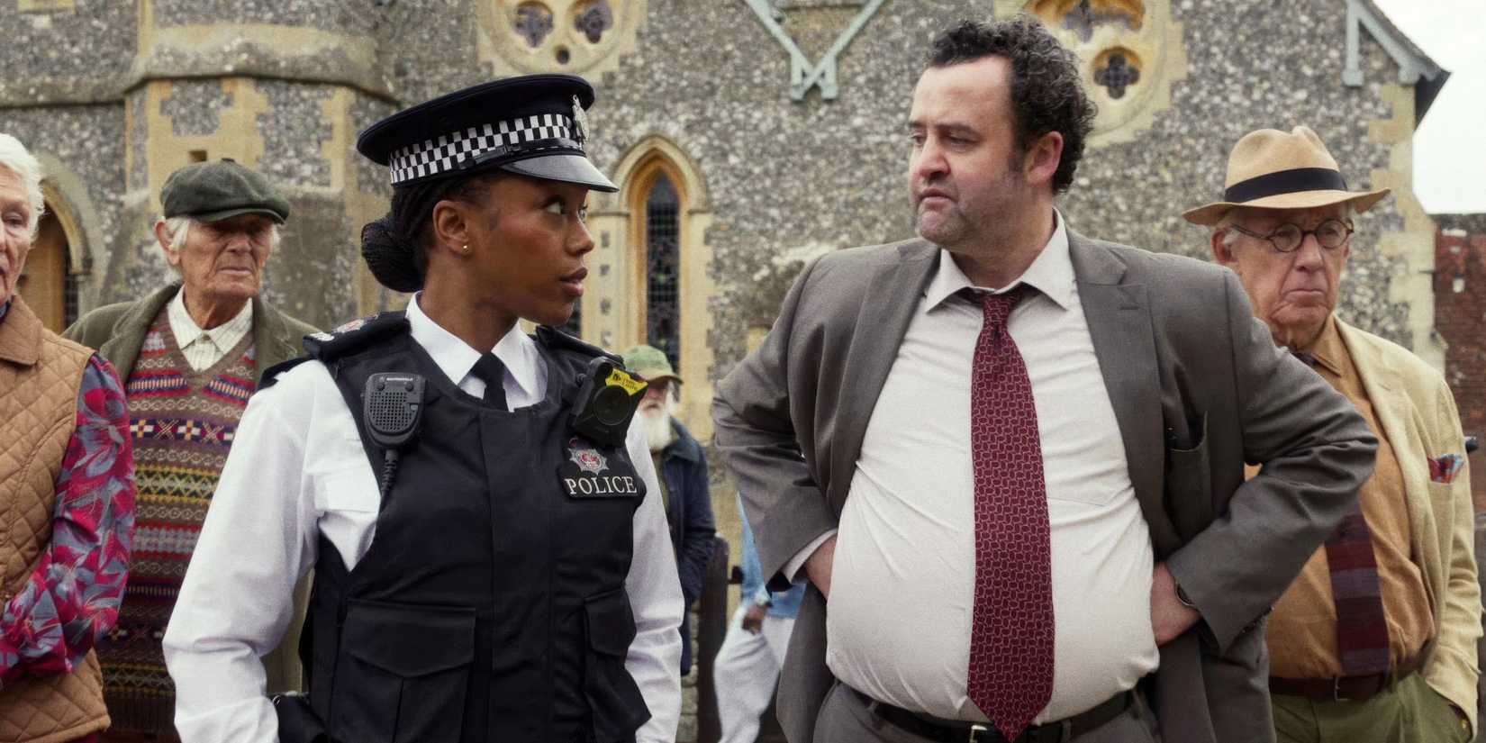 Naomi Ackie and Daniel Mays looking at each other while standing among senior citizens in The Thursday Murder Club