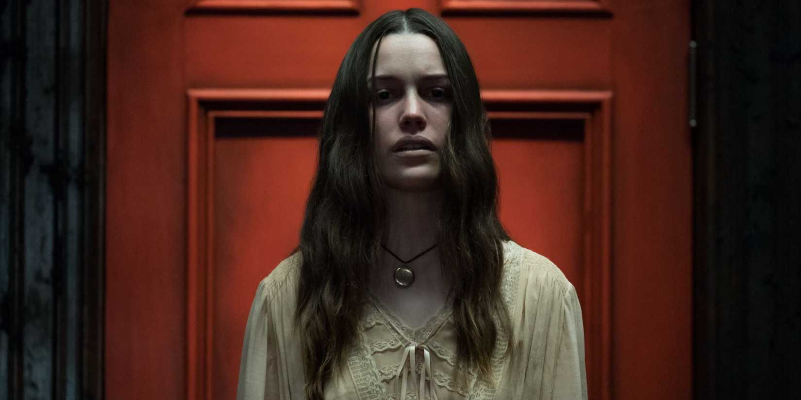 Nell (Victoria Pedretti) standing in front of a red door in a trance in The Haunting of Hill House.