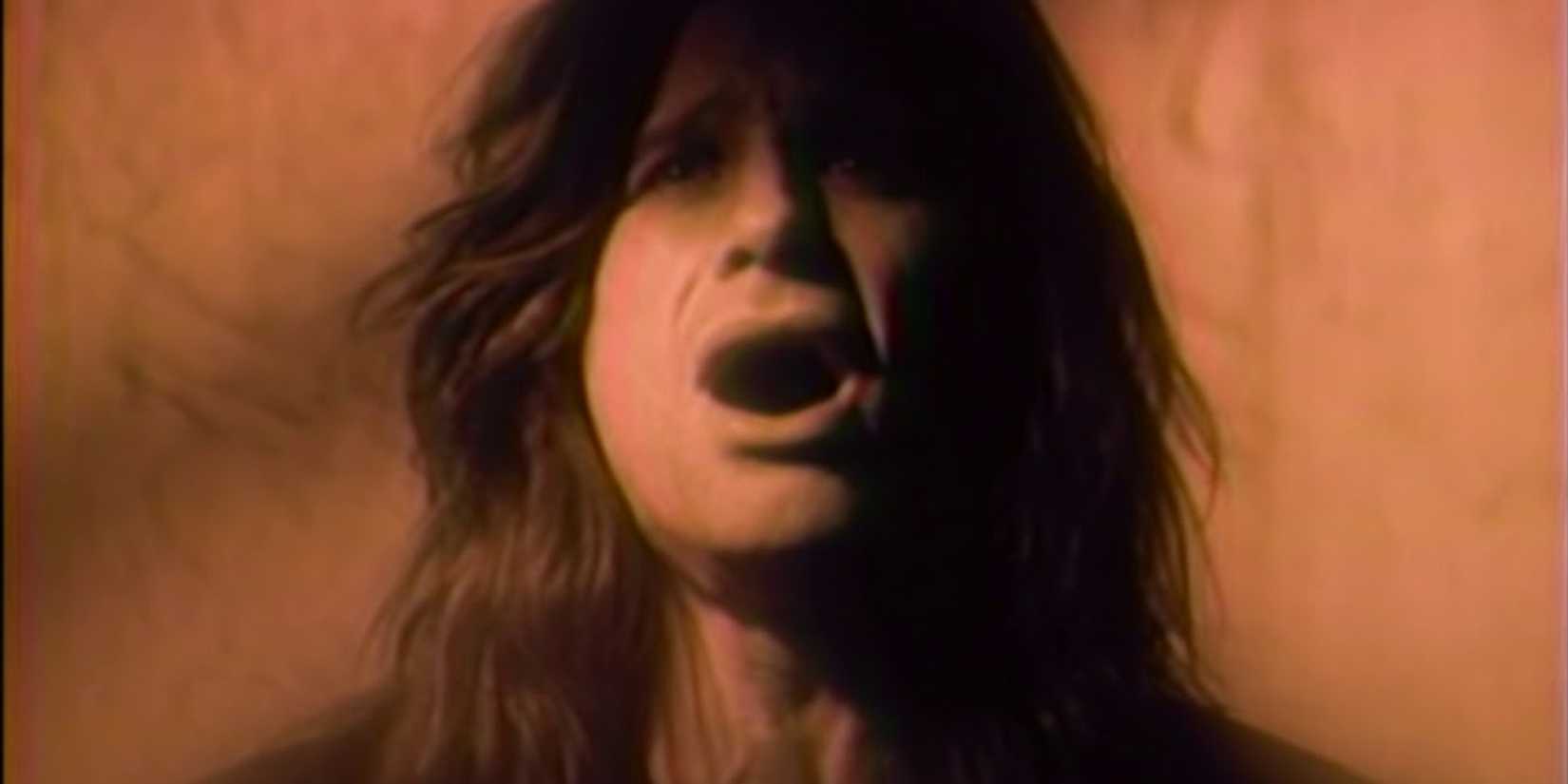 A person with long hair is depicted singing passionately against a warm, sepia-toned background. Their expression conveys intensity and emotion.