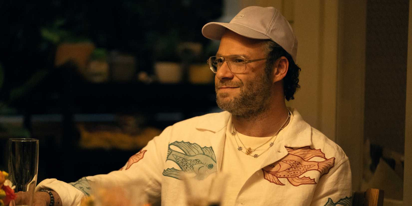 Will, played by actor Seth Rogen, sits at a table and smiles while looking to the side in in Apple TV+'s Platonic season 2