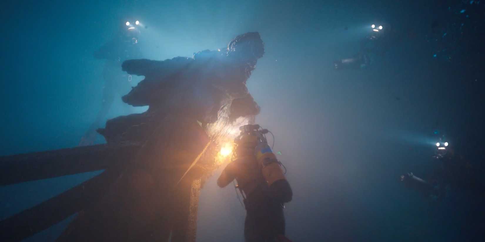 Four divers surround an ancient statue underwater in Play Dirty