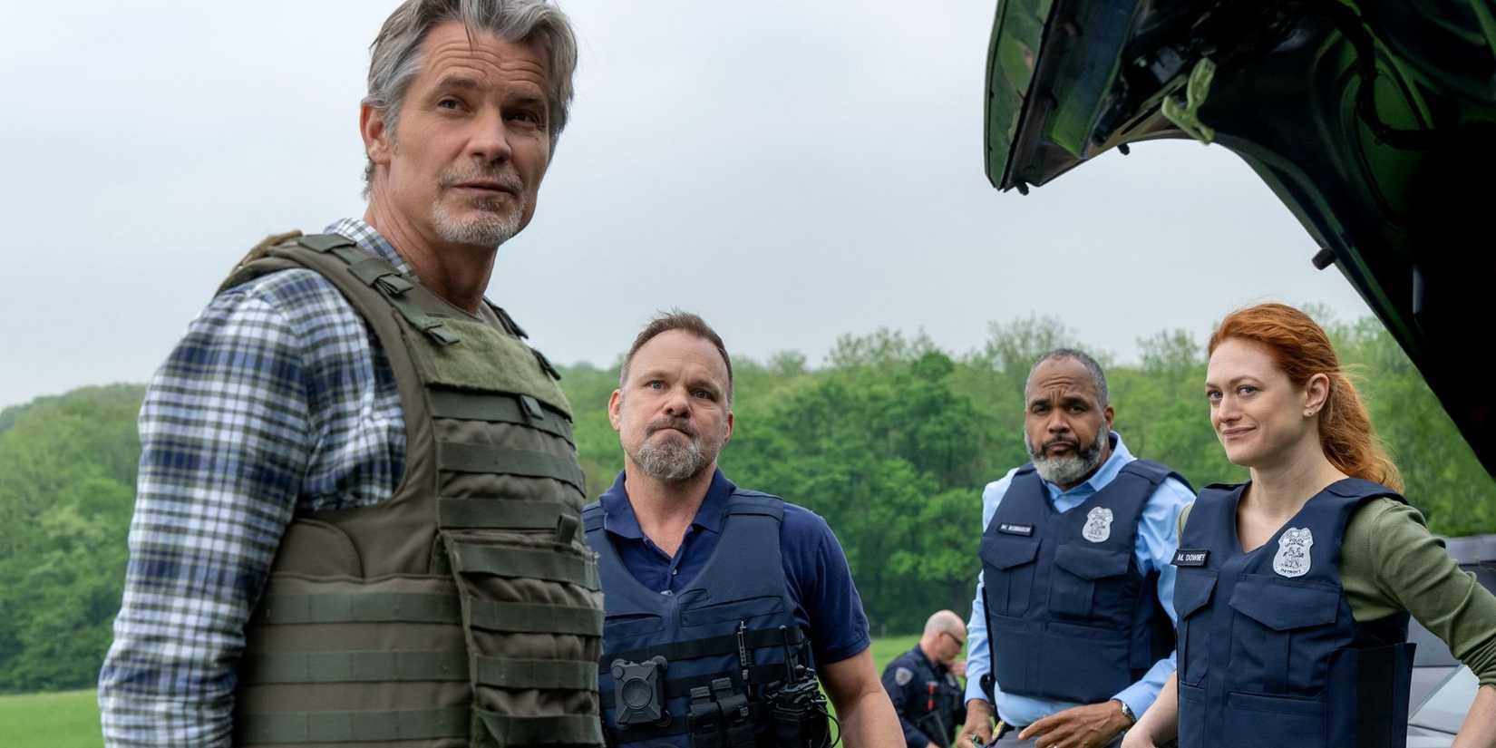 Timothy Olyphant Timothy Olyphant, Norbert Leo Butz, Victor Williams, Marin Ireland, all staring forward toward something off-screen, smirks on their faces, huddled around an open car trunk in Jus