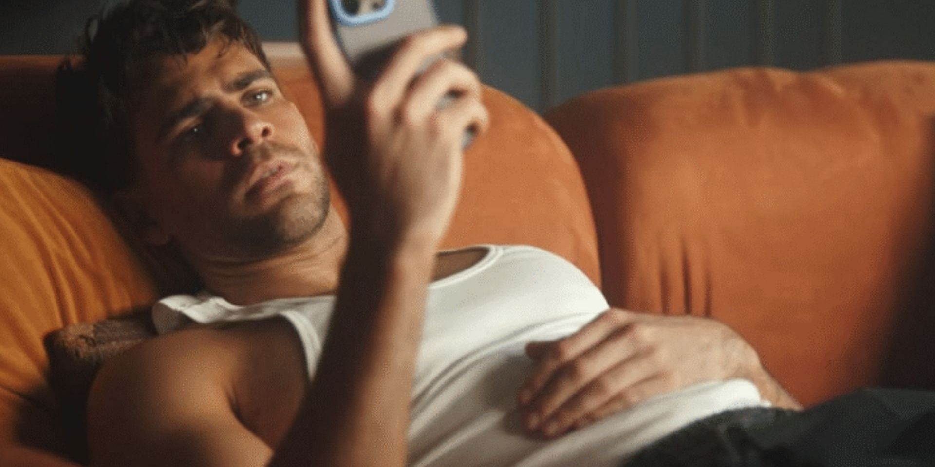 Character sitting on a couch and looking at his phone in Unspeakable Sins