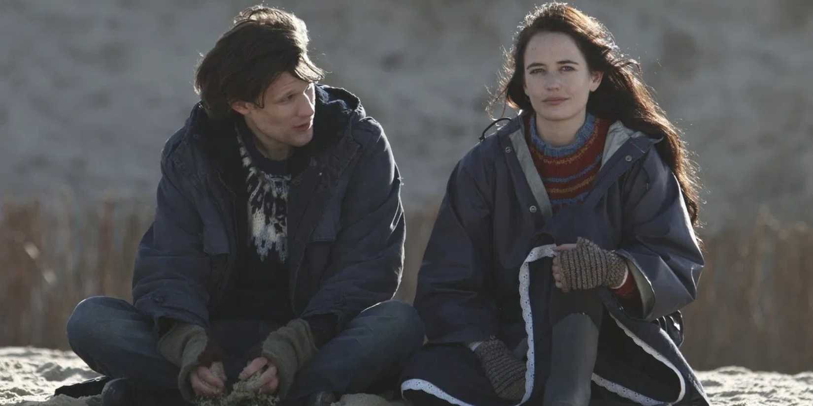 Eva Green as Rebecca and Matt Smith as Tommy sitting together on a hill top with big jackets on in Womb.