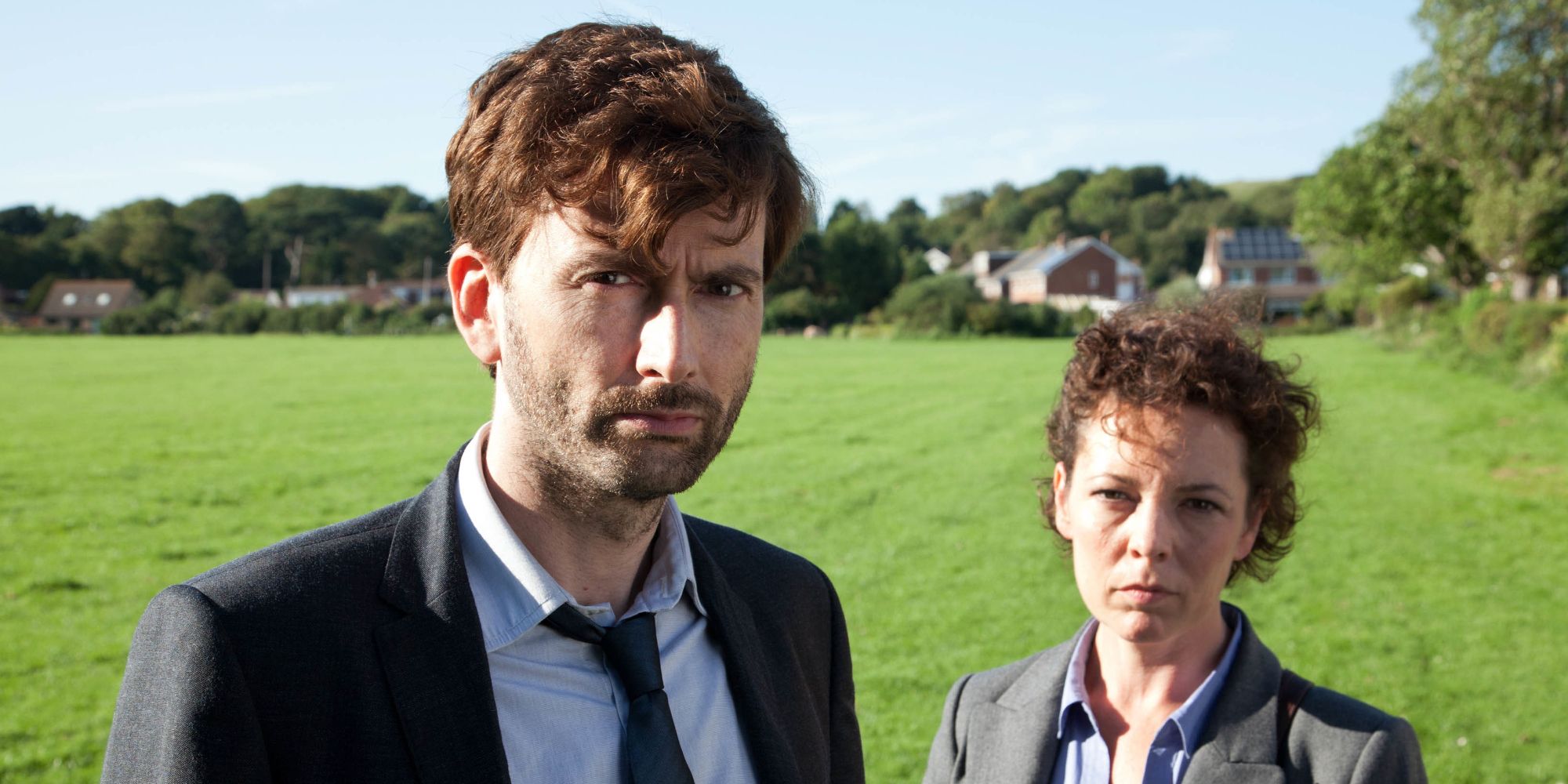 David Tennant como Alec Hardy e Olivia Colman como Ellie Miller em um campo, olhando direto para a câmera, em Broadchurch.