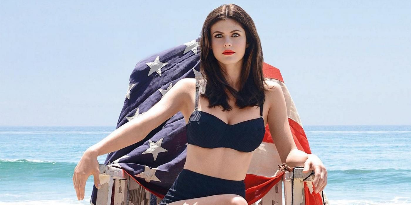 Alexandra Daddario sits on a lifeguard chair with an American flag on it in Baywatch