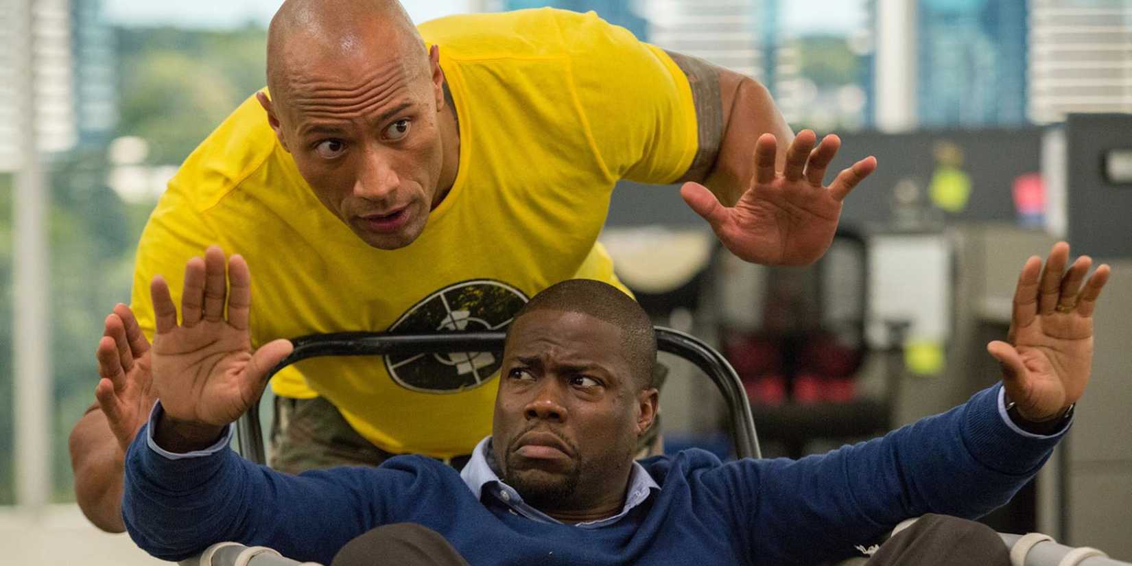 Dwayne Johnson and Kevin Hart raise their hands while the latter is in a cart in Central Intelligence