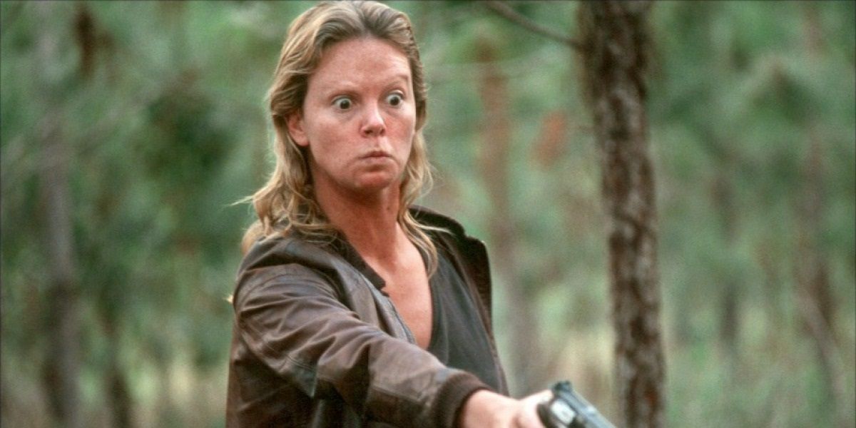 Aileen Wuornos (Charlize Theron) menaces someone with a gun in the woods from Monster