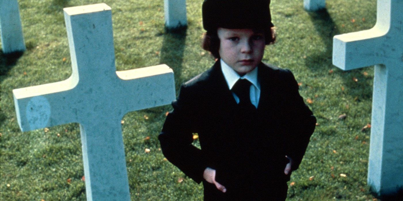 Damien Thorn in The Omen (1976) stands in front of gravestone