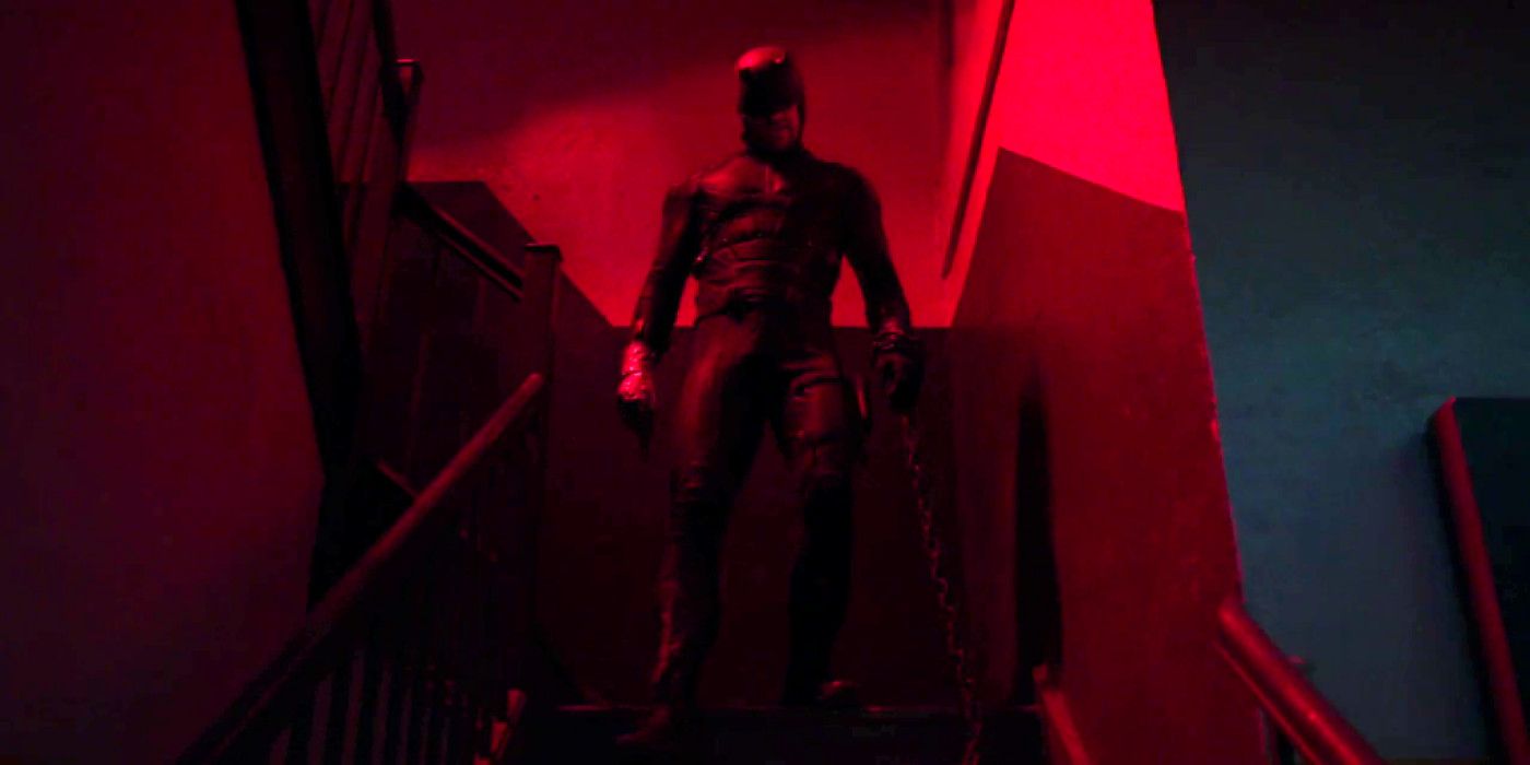 Demolidor em cima de uma escada em uma sala com luz vermelha.