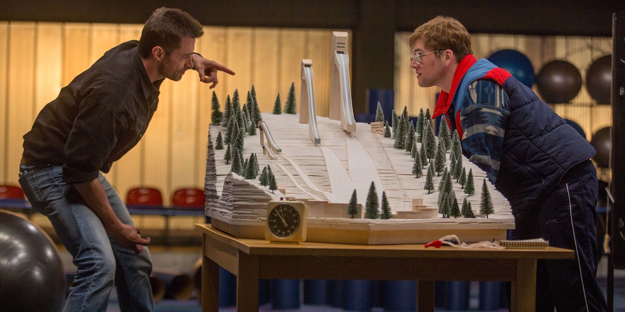 Bronson Peary (Hugh Jackman) and Eddie the Eagle (Taron Egerton) looking at a model of the ski jump.
