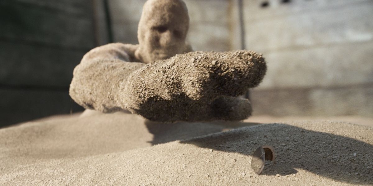 Sandman estende a mão para pegar um medalhão na areia em Spider-Man 3 Sandman