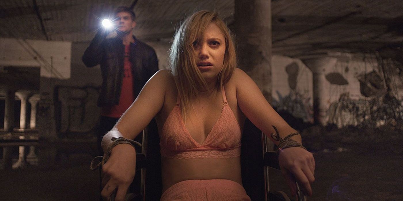 Jay tied to a chair as Hugh stands behind her with a flashlight in It Follows