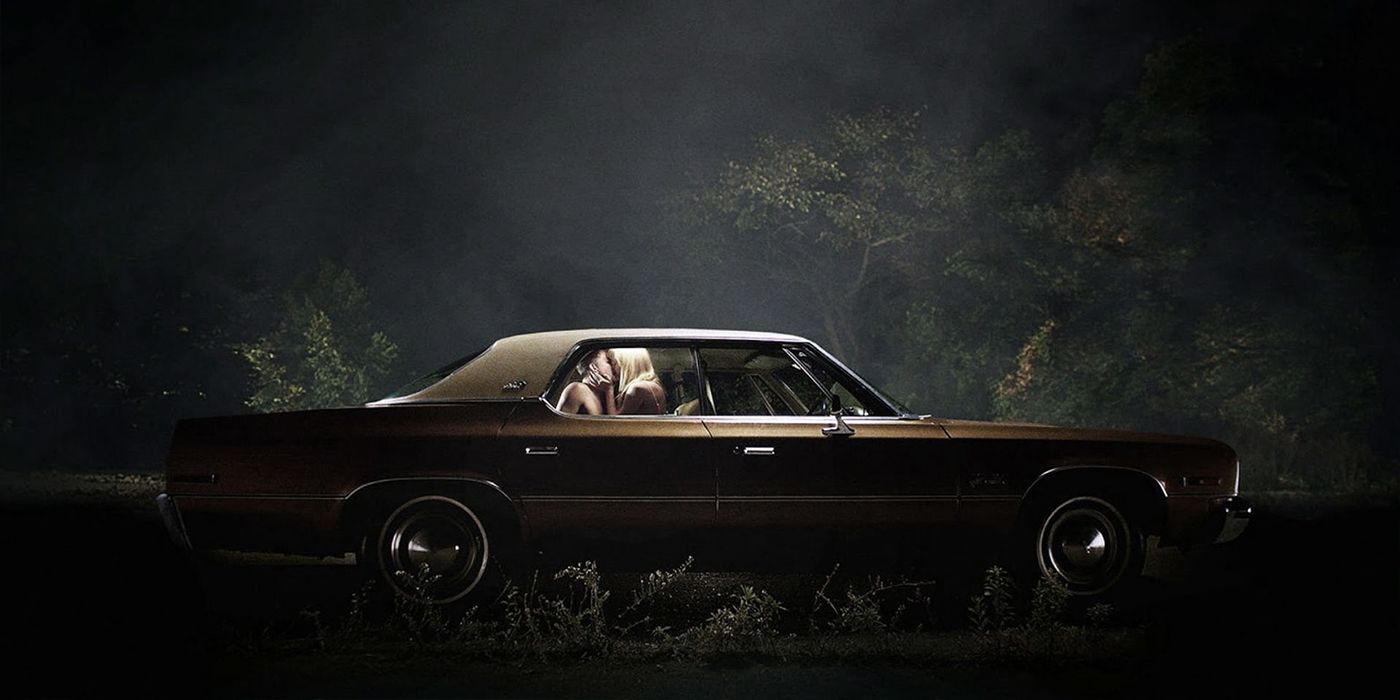 A car in a wooded area at night with a couple making out inside in It Follows.