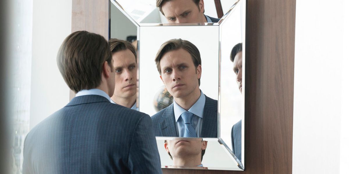 A man in suit looking at himself in a mirror with his reflection on all sides in a scene from Mr. Robot.