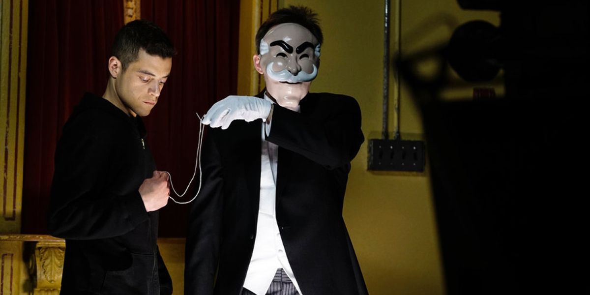 Elliott with a masked character in a suit ready to record an fsociety video in Mr. Robot.