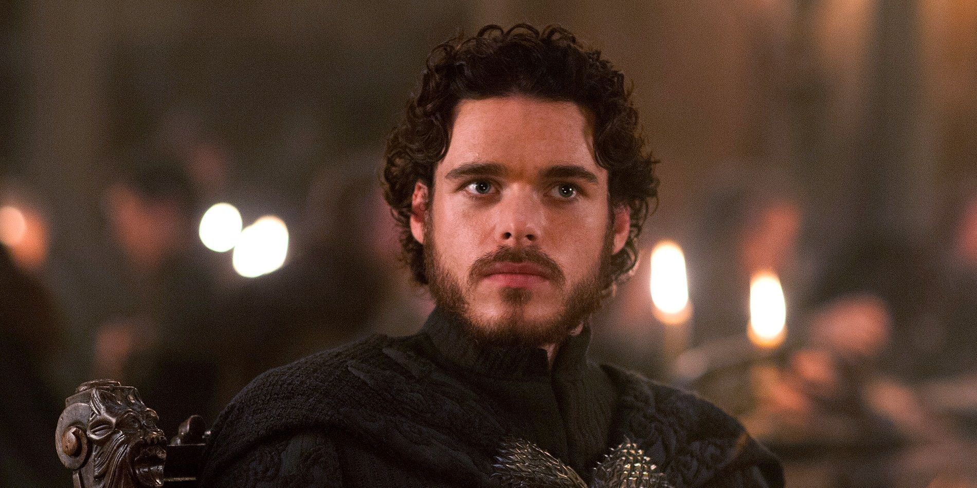 Robb Stark olhando atentamente em uma sala cheia de pessoas em Game of Thrones.