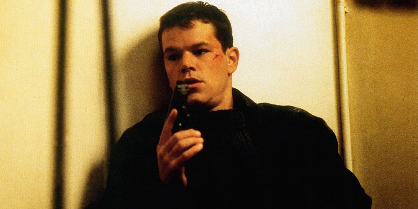Matt Damon as Jason Bourne in The Bourne Identity hiding behind a wall with a gun