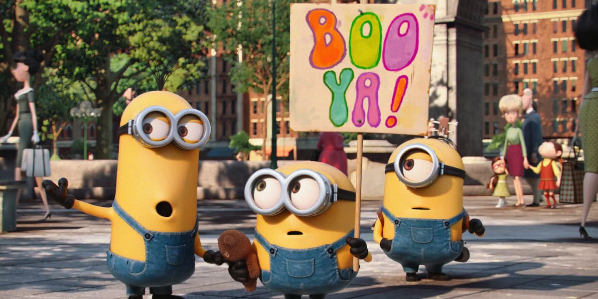 Three minions in the street with a sign in Minions