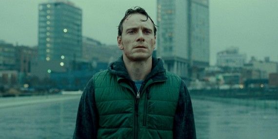 Michael Fassbender standing in the rain with buildings behind him in Shame