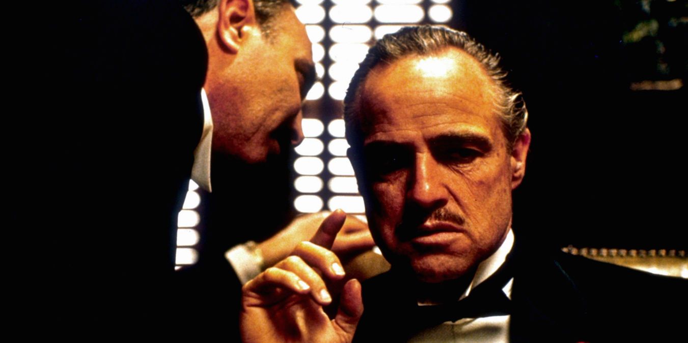 Um homem sussurrando no ouvido de Vito Corleone em O Poderoso Chefão.