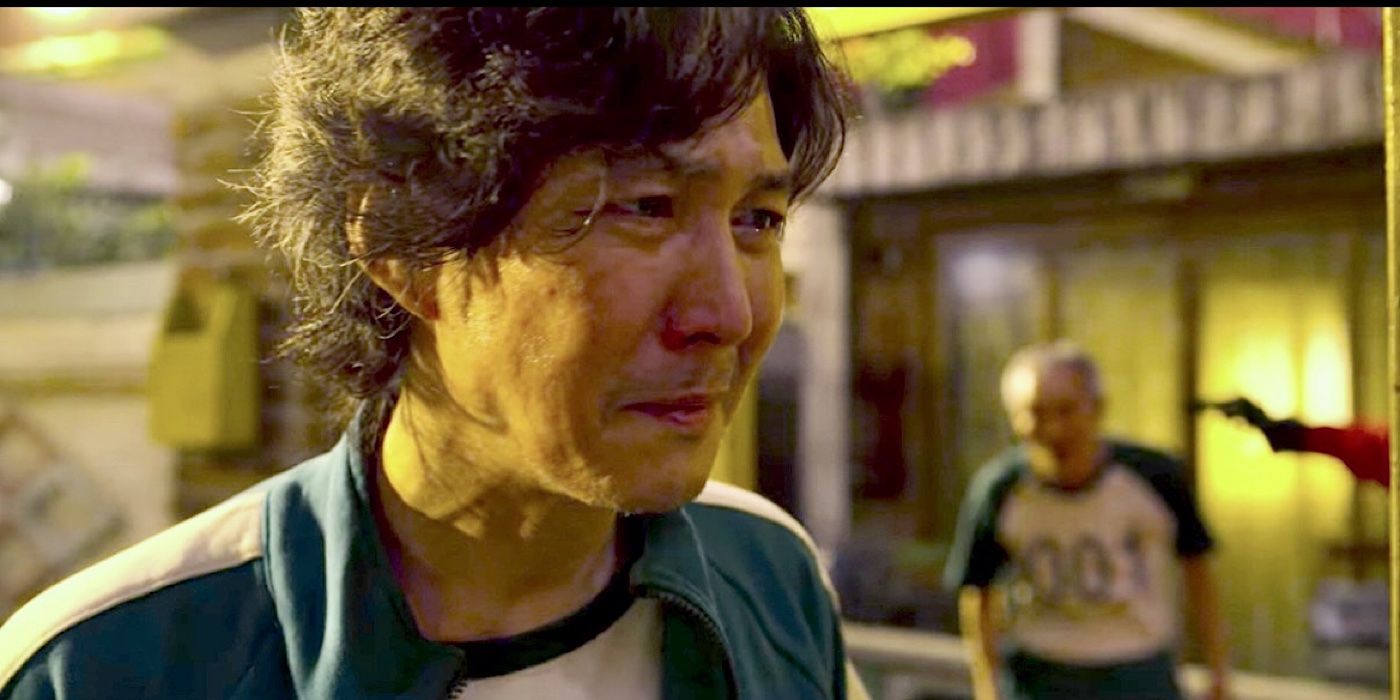 Gi-hun has tears in his eyes as II-Nam has a gun to his head behind him in Squid Games. - Squid Game's main character will have to be clever to pull this off - Gi-hun Will Secretly Enter Another Squid Game
